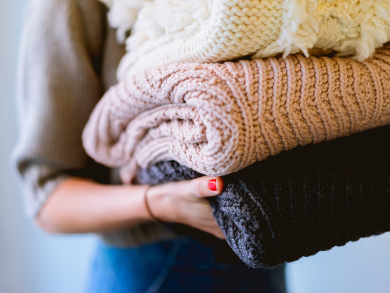 a woman holds a pile of pink, grey and white blankets in her hands